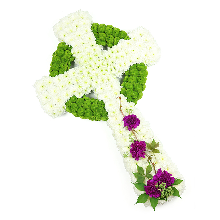 A large, elegant Celtic cross made from fresh flowers is displayed horizontally against a pristine white backdrop, every element clearly visible as though you are standing beside the workbench in a Tolworth flower shop. The form of the cross is generous and well-defined, with the main vertical stem and crossbar completely covered by a thick layer of small white chrysanthemums. These blooms, closely packed and uniformly arranged, create a smooth but softly textured blanket of petals that speak of purity and serenity. Interlaced within this white field is an intricate Celtic pattern picked out in lime-green button chrysanthemums. Their compact, spherical heads are arranged with precision to form the circular ring at the centre, as well as the knot-like bands running along the arms and stem. This vibrant green threading gives structure and rhythm to the design, calling to mind the ancient Celtic symbols of eternity and faith, themes that often resonate with families in the Tolworth area when choosing a funeral tribute. On the lower part of the vertical arm, three lush clusters of deep purple carnations bring a poignant depth of colour. Their ruffled petals, layered and slightly curled at the edges, add a sense of movement and tenderness that contrasts with the discipline of the Celtic patterning. Around and between the carnations, slim strands of dark green foliage and curling tendrils of vine are woven lightly across the chrysanthemums, softening edges and adding an organic, almost windswept feel, reminiscent of greenery found in nearby parks and churchyards. The lighting is soft but bright, with minimal shadow, accentuating every petal and texture. It is a dignified, heartfelt floral cross, well suited for a church, crematorium, or graveside service in and around Tolworth, where it would serve as a meaningful symbol of remembrance and enduring love.
