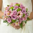 Bathed in soft natural light, this bridal bouquet evokes a feeling of joyful anticipation, blending lilac roses, pink alstroemeria, and zesty green button chrysanthemums in a graceful, harmonious dance. Each velvety rose opens with a promise, releasing the faint scent of spring mornings, while the bright green mums dot the arrangement with modern verve. Subtly streaked alstroemeria contribute complexity and movement, their petals flecked with golden and maroon patterns that hint at exotic travels or carefree Tolworth afternoons in local parks. Wispy sprays of white gypsophila lend an airy softness, gently enveloping the blooms and enhancing their serenity. The bouquet is cradled lovingly by a bride in a pristine gown, hands steady yet brimming with excitement-ready to begin a new chapter at a beloved Tolworth venue. Lush green leaves frame the flowers, mirroring the leafy calm of Alexandra Recreation Ground. This arrangement, designed by expert florists, feels like a fresh beginning captured in color and texture, destined to witness treasured vows and joyful celebrations in Tolworth's vibrant community. Its mood is serene yet hopeful, perfect for a spring or summer wedding filled with love and local spirit.